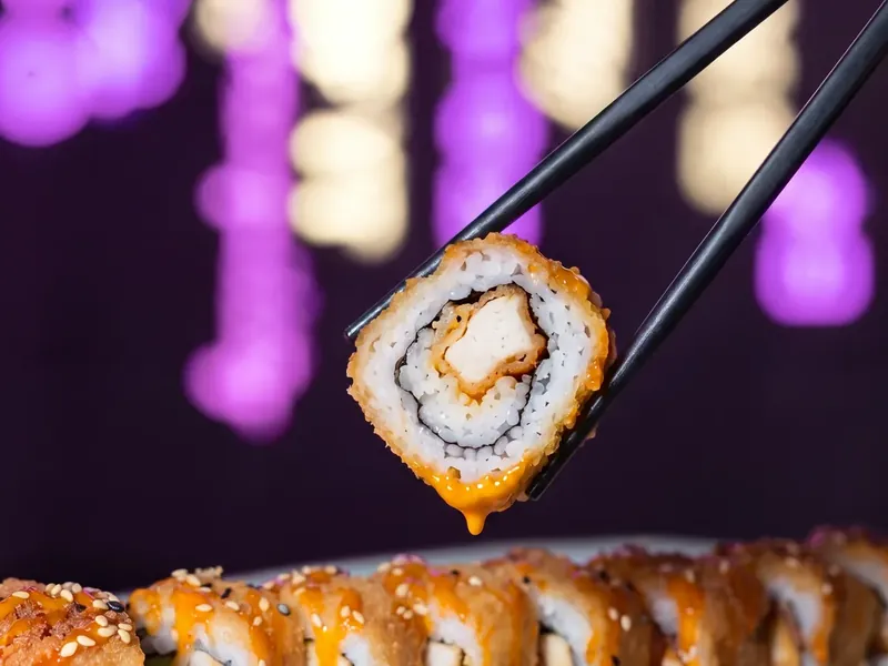 Photo d'un california pané levé aux baguettes au-dessus des rolls sauce épicée chez Yushithaï, le meilleur sushi à Lyon 6, Foch, rue Duguesclin