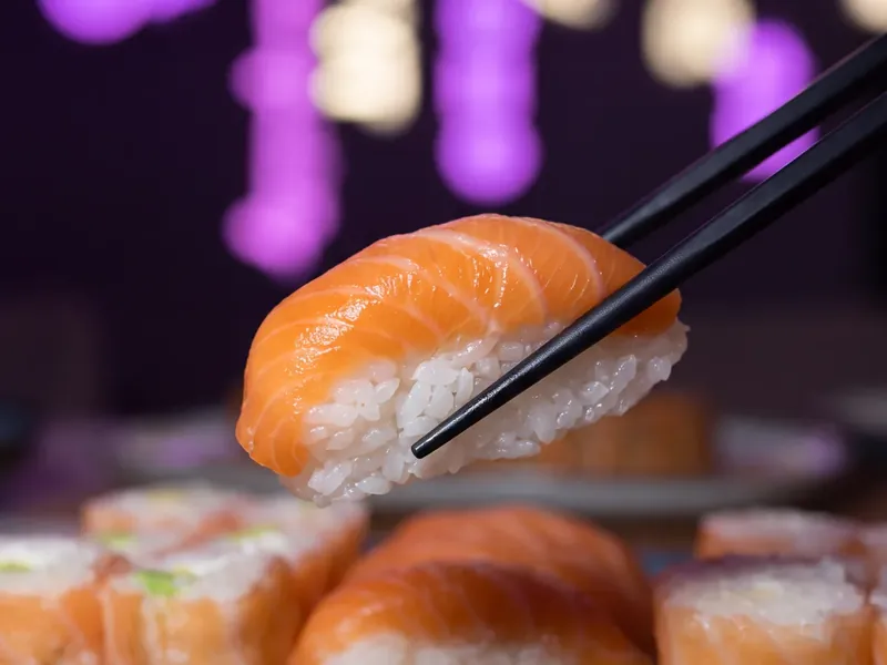 Photo d'un sushi saumon levé aux baguettes sous les néons roses chez Yushithaï, le meilleur sushi halal à Lyon 6, Masséna, à dix minutes de la Part-Dieu