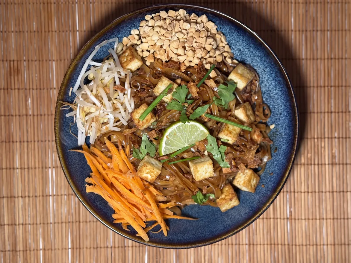 Image d'un pad thaï veggie au tofu vu du dessus, cacahuètes, carottes râpées, pousses de soja et citron vert chez Yushithaï, le meilleur restaurant thaï halal et veggie à Lyon 6, Masséna, près des Brotteaux