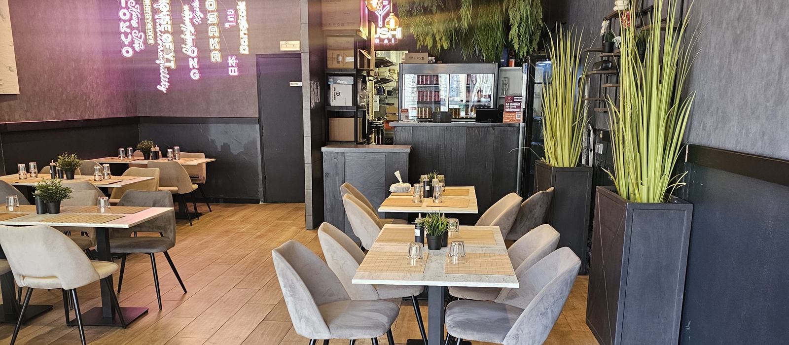 La salle de Yushithaï, ses tables en bois clair et son mur d'enseignes au néon rose