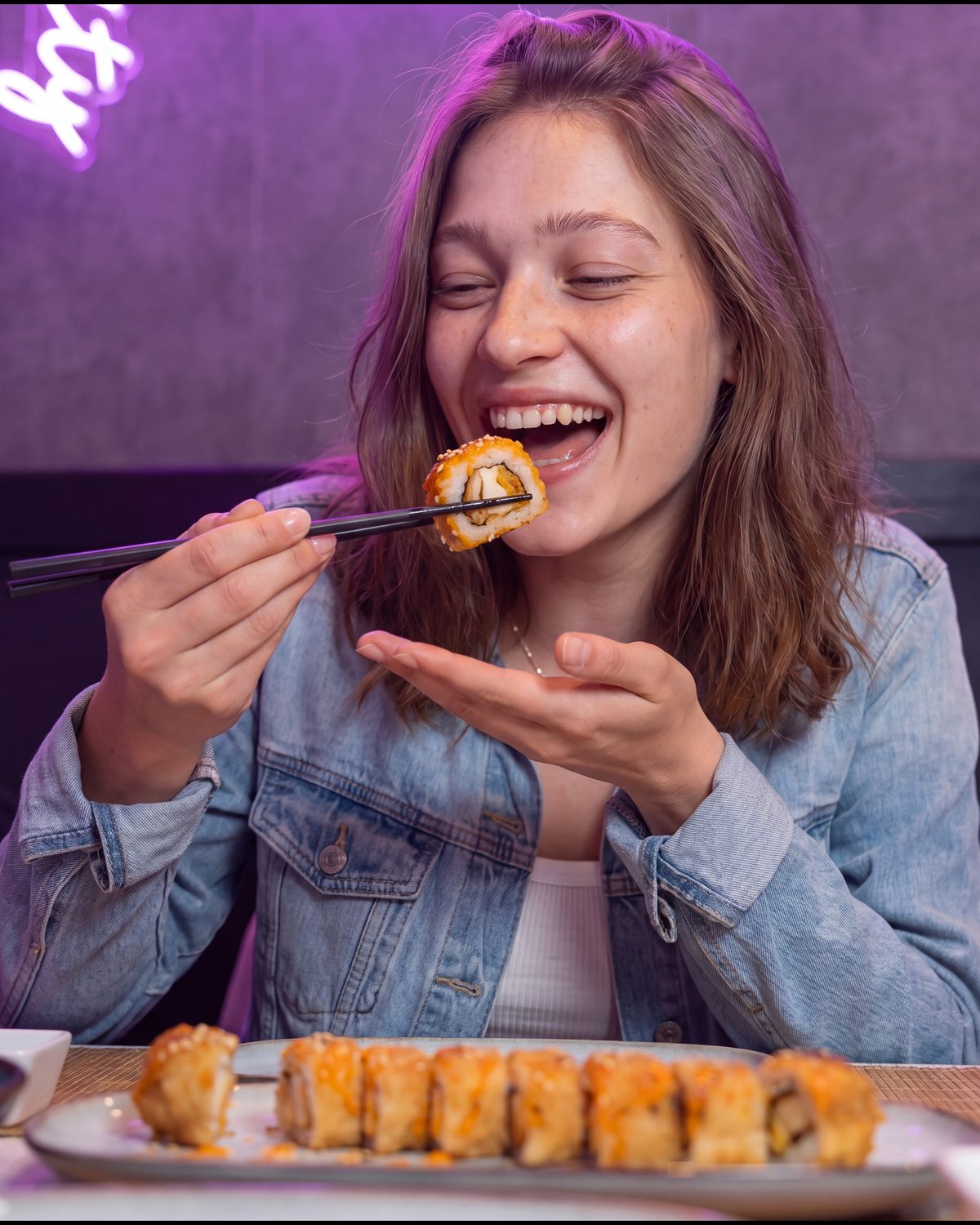Image d'une cliente qui croque un crispy roll pané tenu entre deux baguettes, devant les néons de Yushithaï, le meilleur restaurant halal à emporter à Lyon 6, Brotteaux, rue Duguesclin