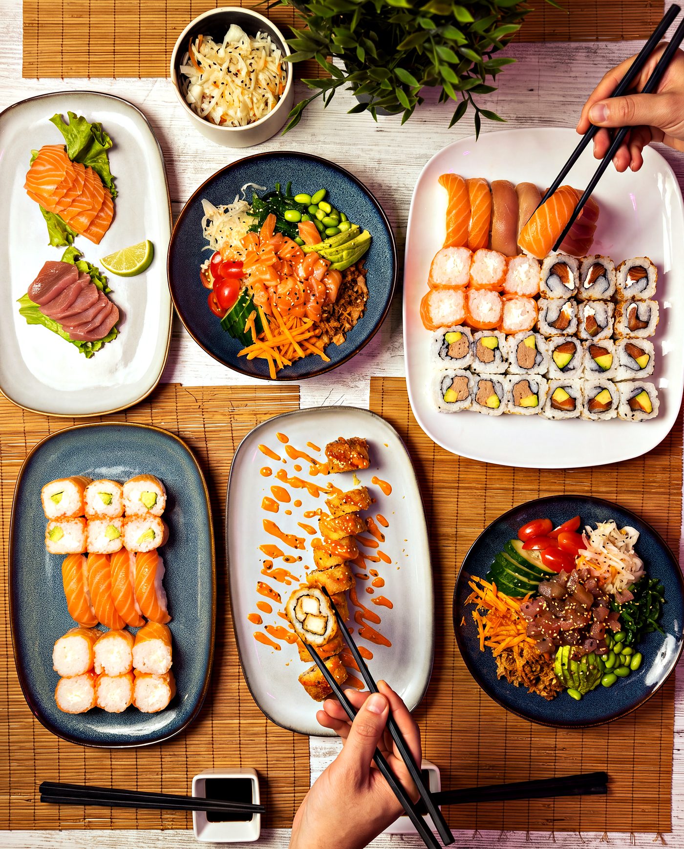 Image d'une tablée vue du dessus, sashimis, poke bowls, plateau de sushis et california pané entre les baguettes, chez Yushithaï, le meilleur restaurant pour les groupes à Lyon 6, Masséna, près de la Part-Dieu